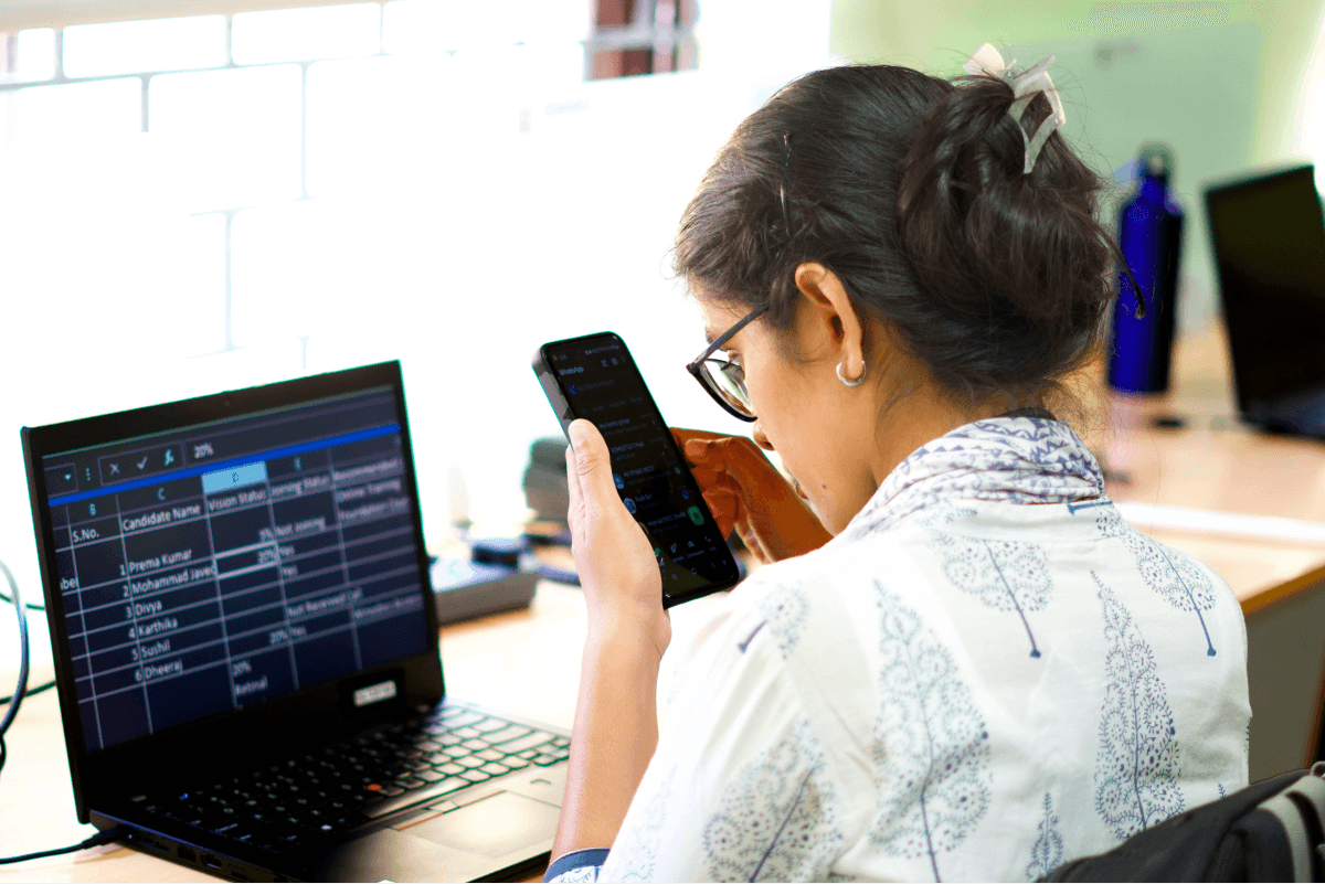 A young woman using screen reader features on a phone while working on a laptop with assistive technology software.