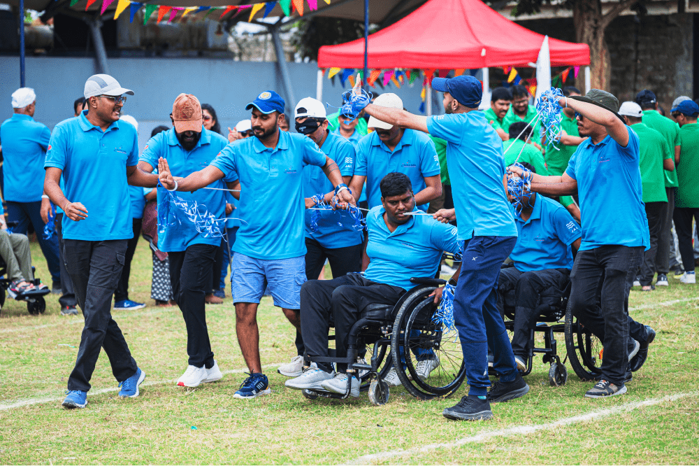 A group of people, including individuals in wheelchairs, participating together in an inclusive outdoor team event on a grassy field.