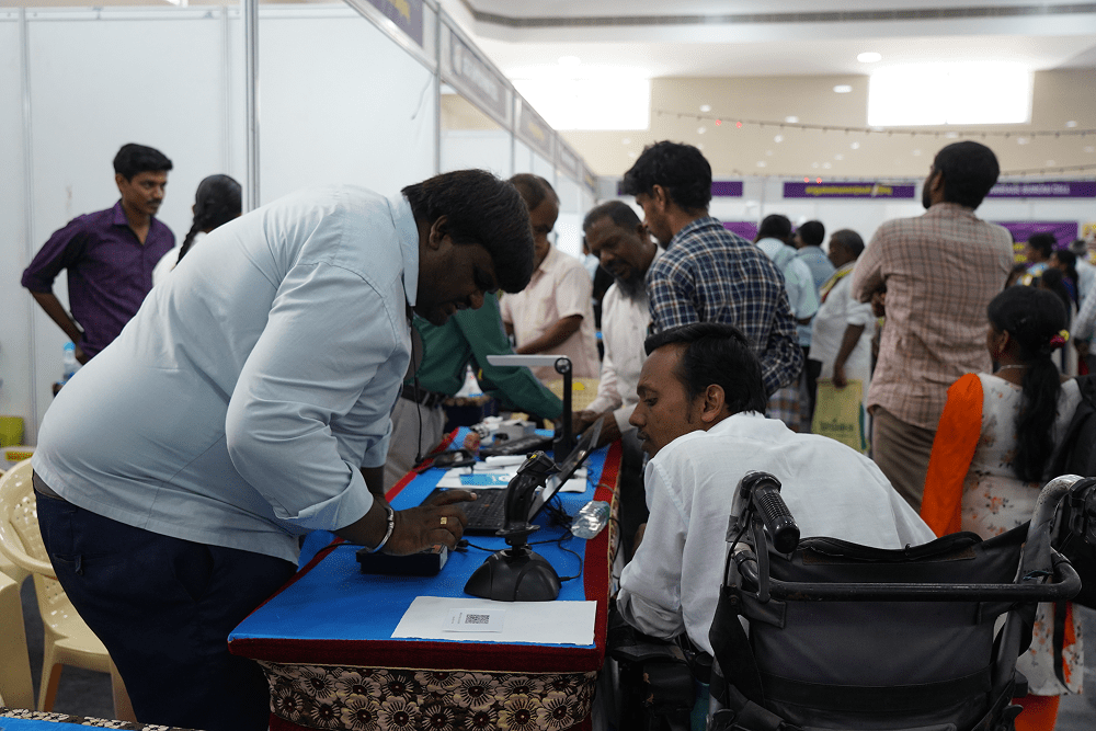An individual with visual impairment, which includes a man in a wheelchair, engaging in a discussion at an event.