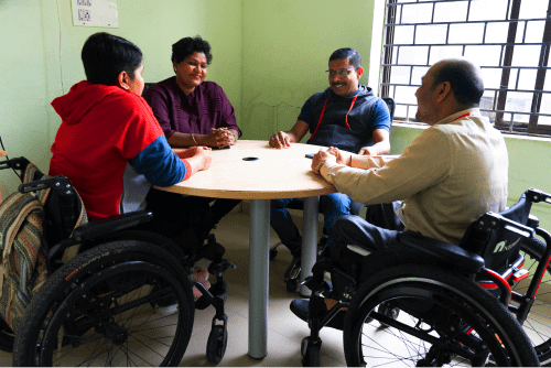 Four people, two in wheelchairs, sitting around a round table in discussion.