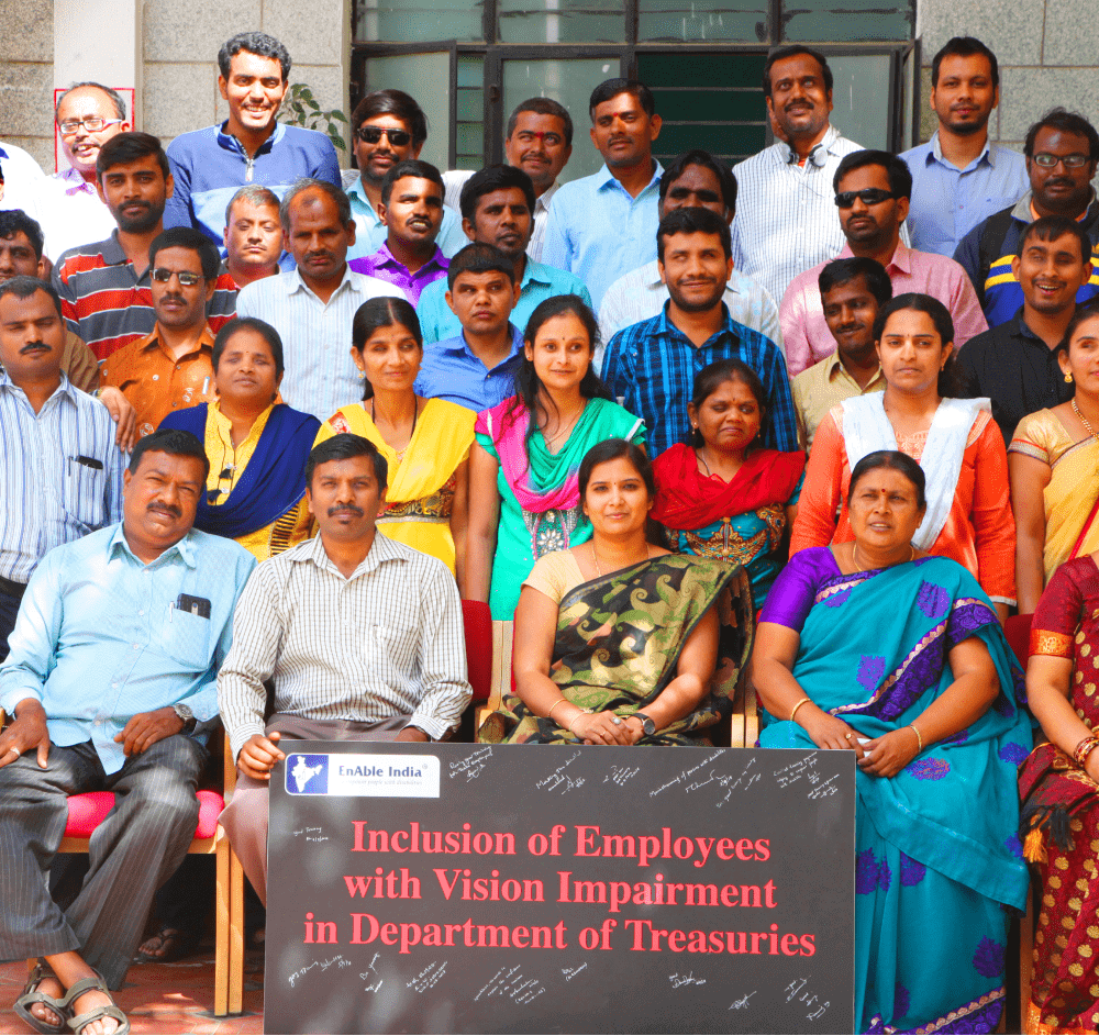 Group photo of government employees, including people with vision impairment, holding a sign about inclusion in the Department of Treasuries.