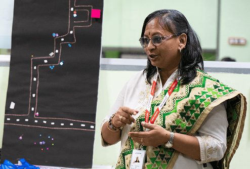 Woman in a green and white shawl presenting a path map chart on a black board.