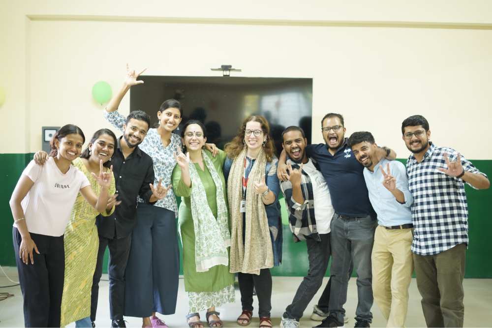 Diverse group of ten people smiling and posing enthusiastically for a photo indoors.