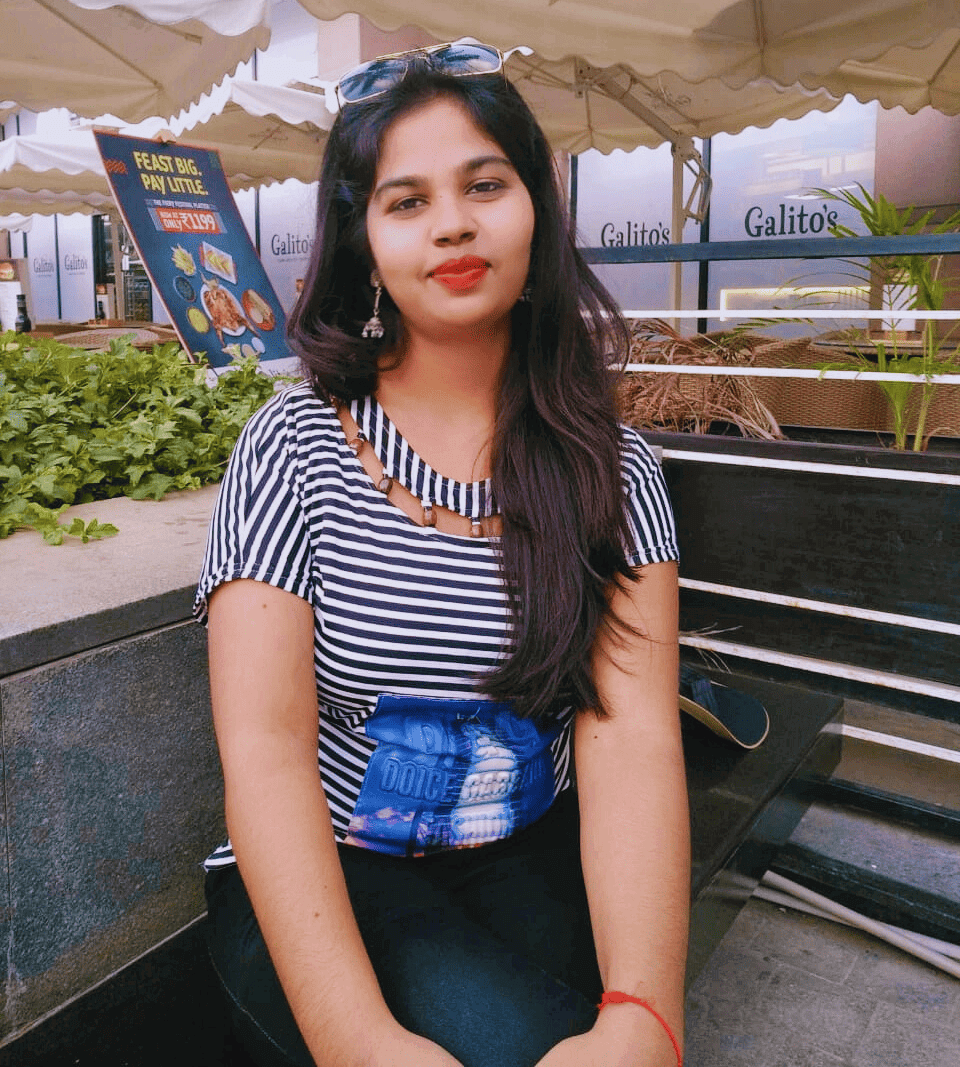 Young woman with long dark hair, wearing a striped shirt and sunglasses on her head, sitting outdoors at a cafe.