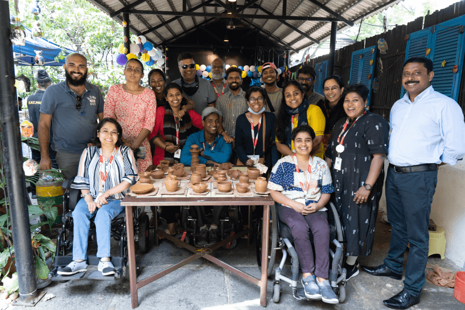Group of seventeen people, including two women in wheelchairs, posing around a table full of terracotta pottery.